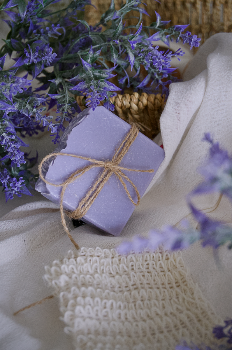 A purple lavender handmade soap laid on some lavender steam and a lofa