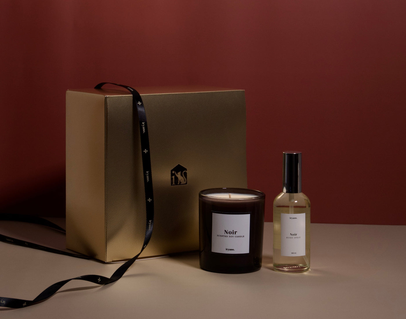 Candle and perfume bottle labeled 'Noir' next to a gold gift box on a brown background