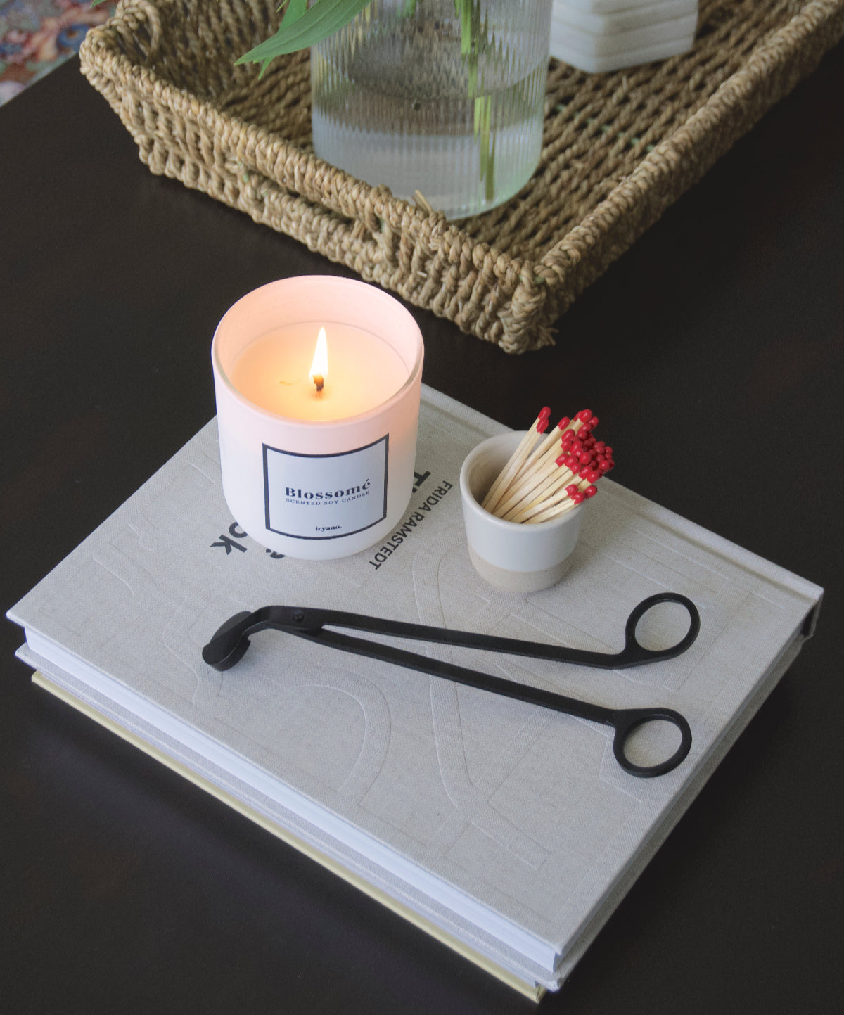 A black wick trimmer, A candle, and some matches in a small jar lay on a book.