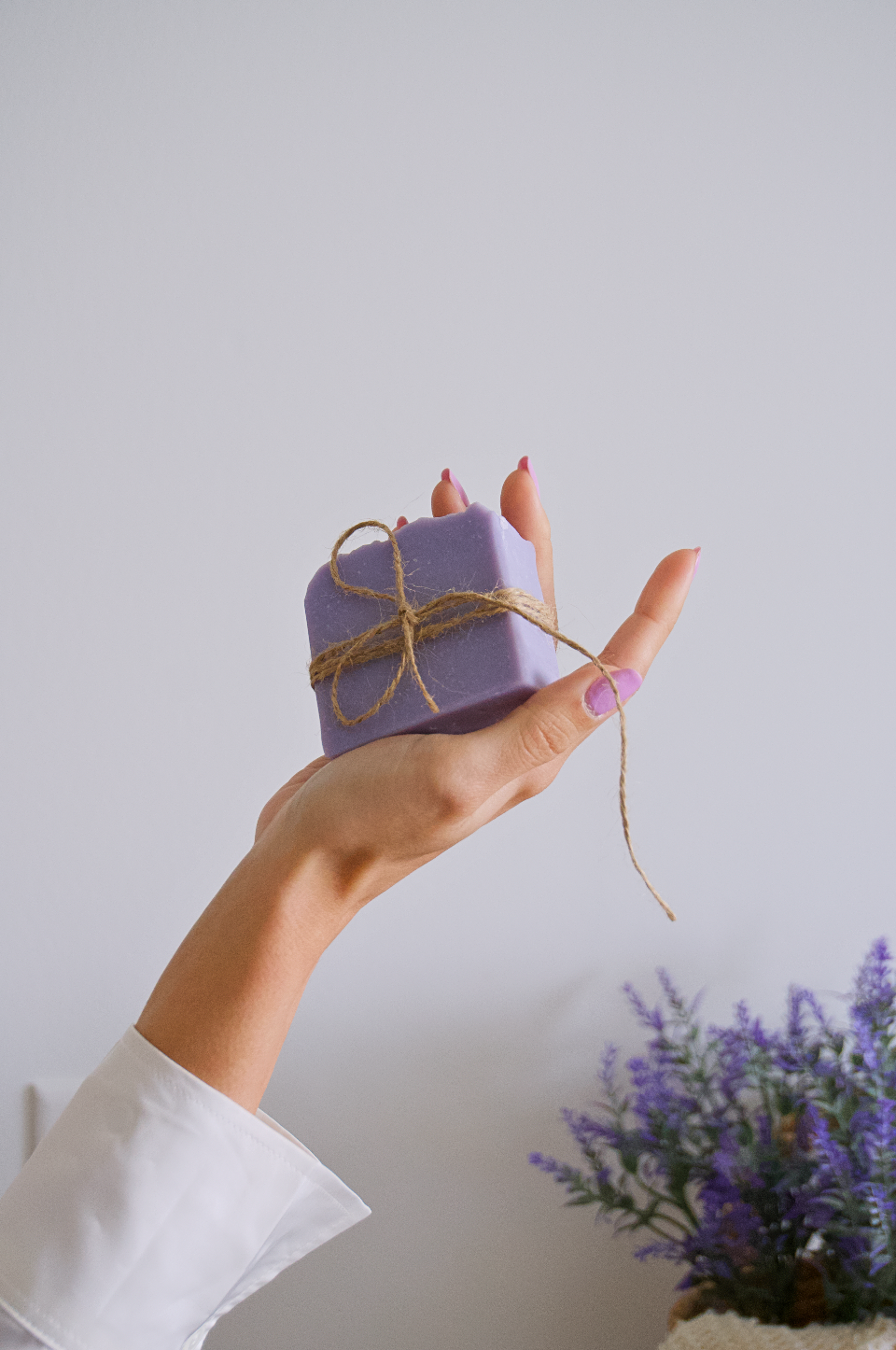 Woman hand holding a lavender soap and lavender steams at the faded background