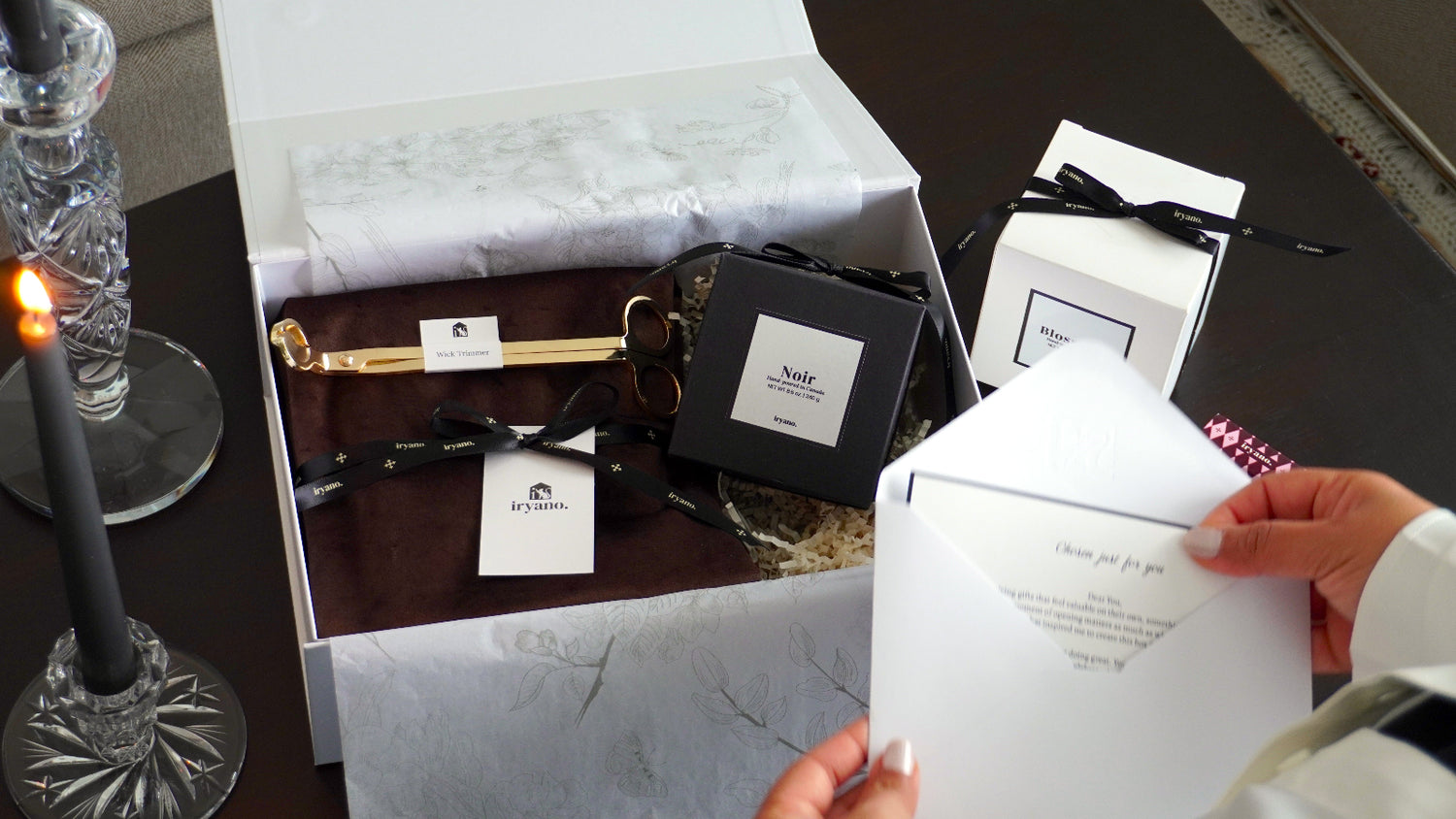 Person holding a white card with a gift box and decorative items on a table.