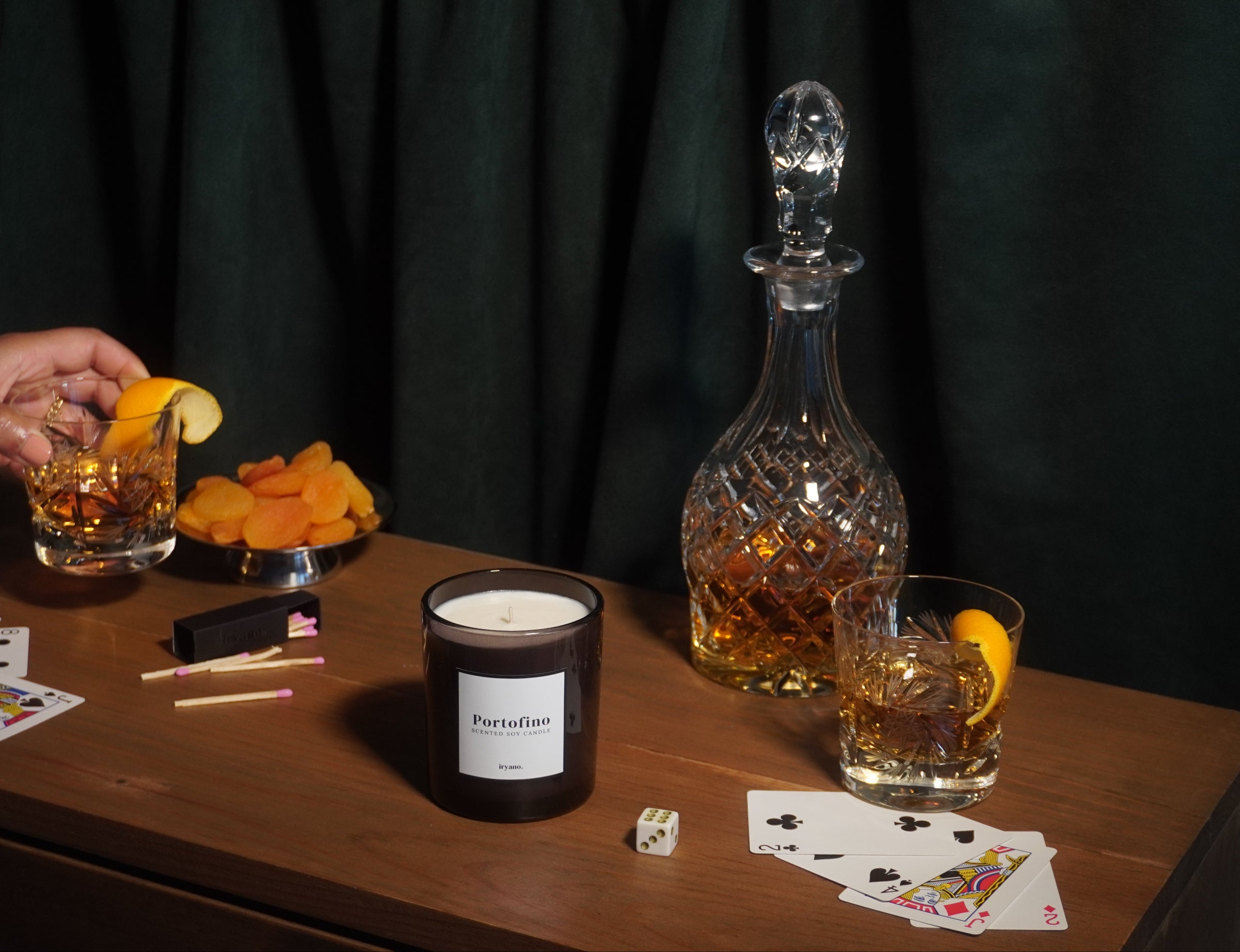 Table with drinks, a candle, and playing cards against a dark curtain background