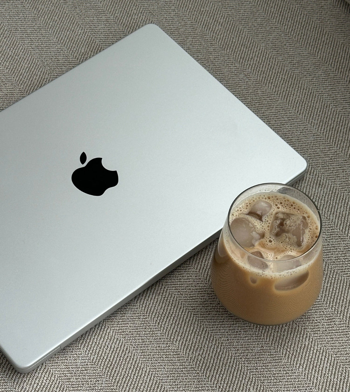 Silver laptop with Apple logo next to a glass of iced coffee on a textured surface