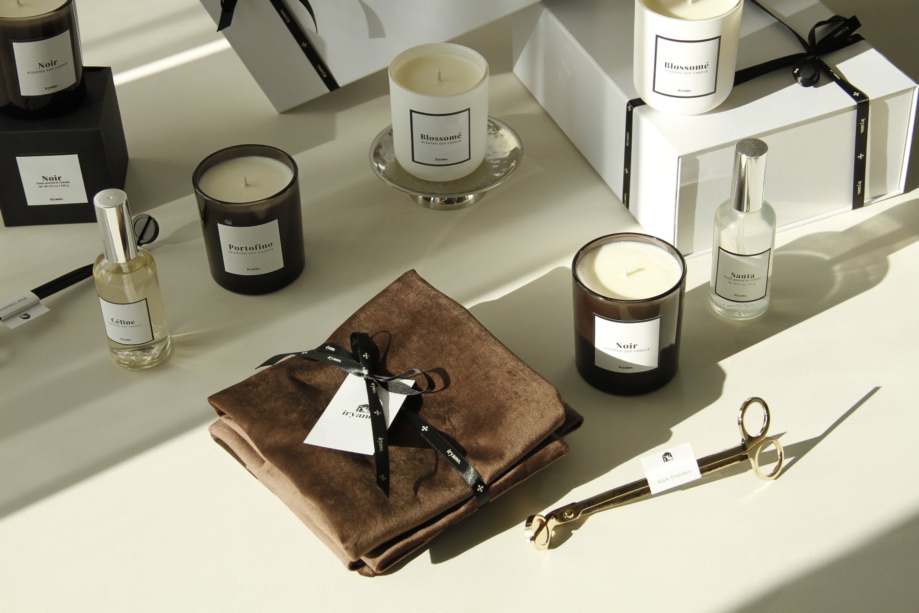 Candles and bottles on a white surface with a brown leather book and gold scissors.