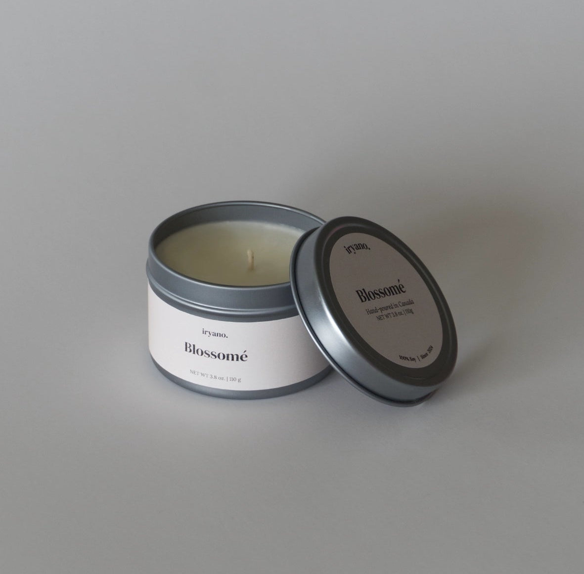 Candle in a metal tin with 'Blossom' branding on a gray background
