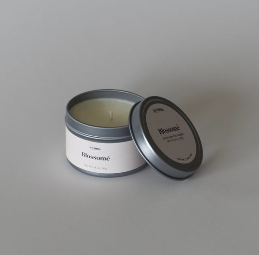 Candle in a metal tin with 'Blossom' branding on a gray background