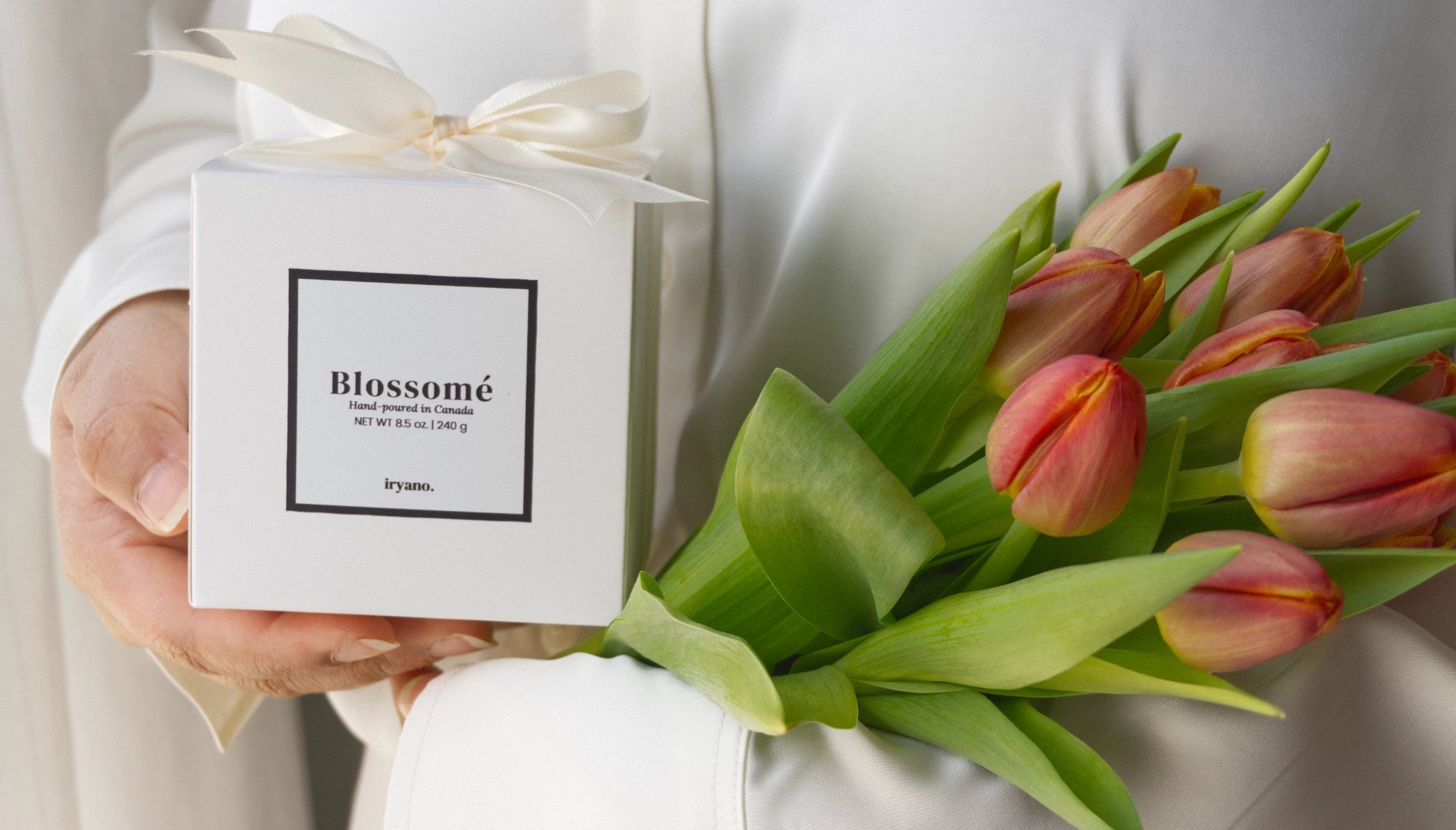 Person holding a bouquet of tulips and a box labeled 'Blossomé' against a neutral background.