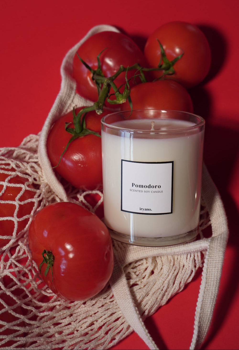 Candle with a label surrounded by tomatoes on a red background