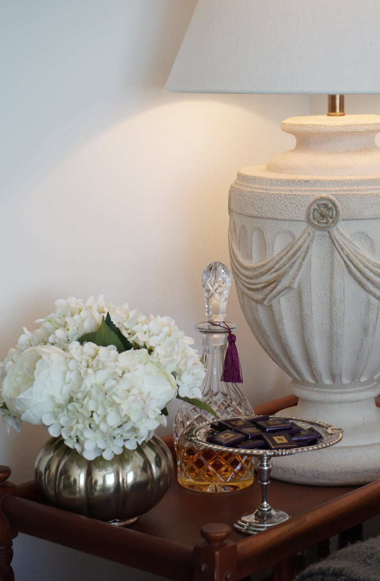 Decorative table setting with flowers, crystal vase, and candle on a white surface.