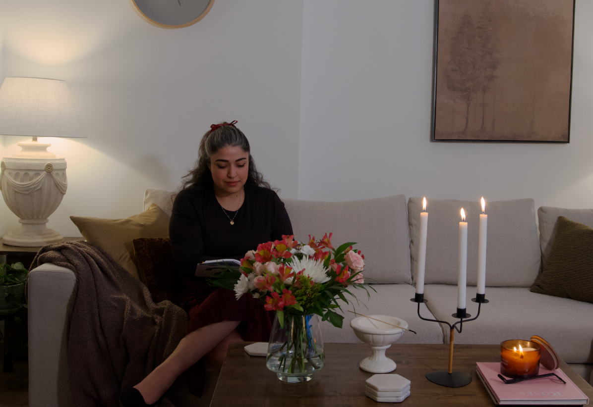 Woman sitting on a couch in a living room with candles and flowers on a table.