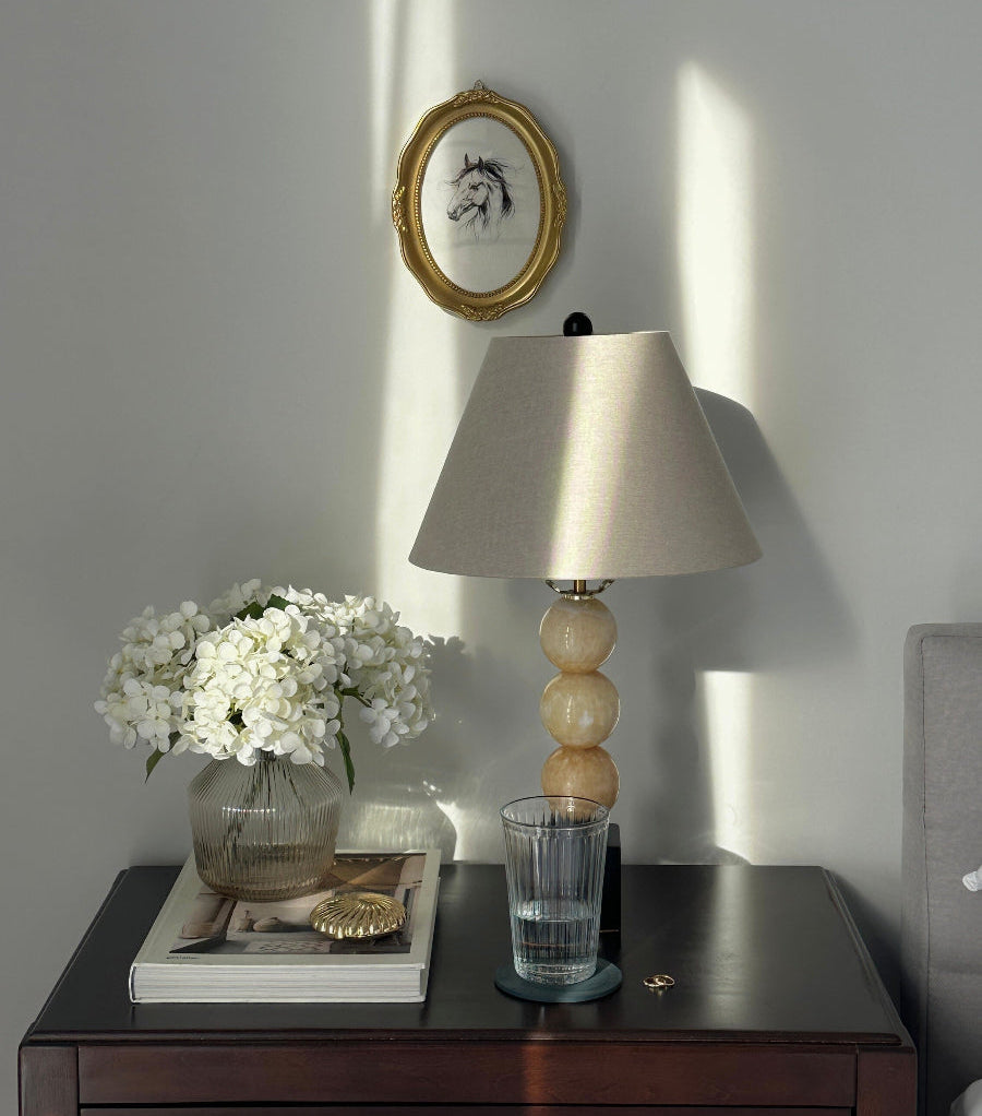 Nighstand with lamp, vase of flowers, and framed pictures on a wall.
