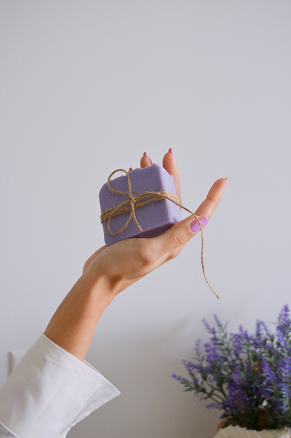 Woman hand holding a lavender soap and lavender steams at the faded background